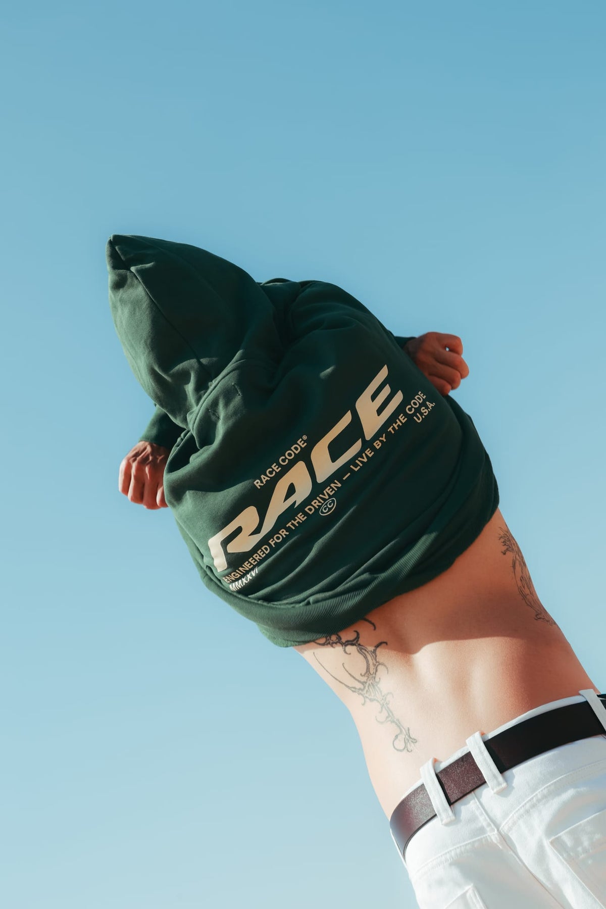 Model wearing Race Hoodie Green, back view against a blue sky