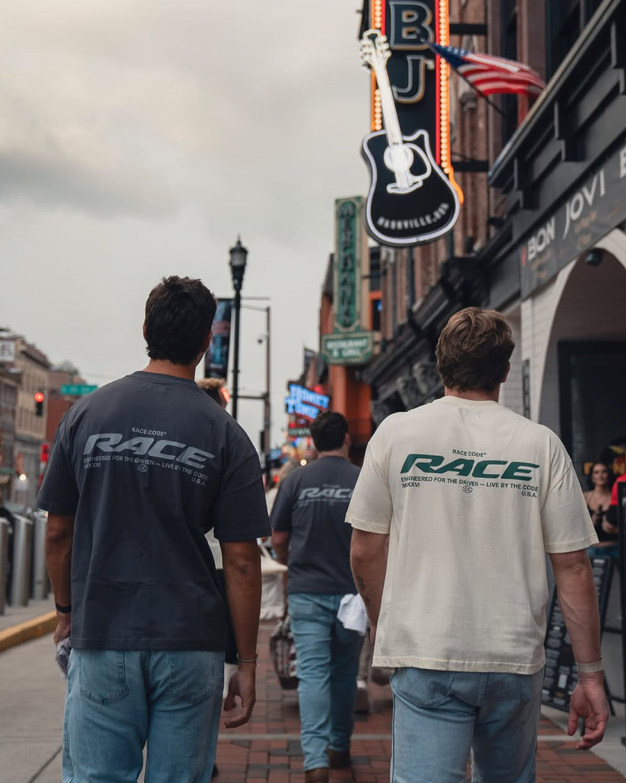 Modelos con la Race Tee Cream y la Race Tee Dark Grey, vista trasera en una calle de la ciudad