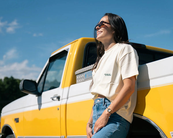 Woman leaning against a yellow and white truck on a sunny day