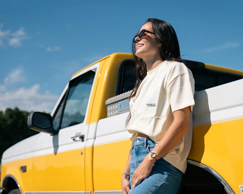 Woman leaning against a yellow and white truck on a sunny day