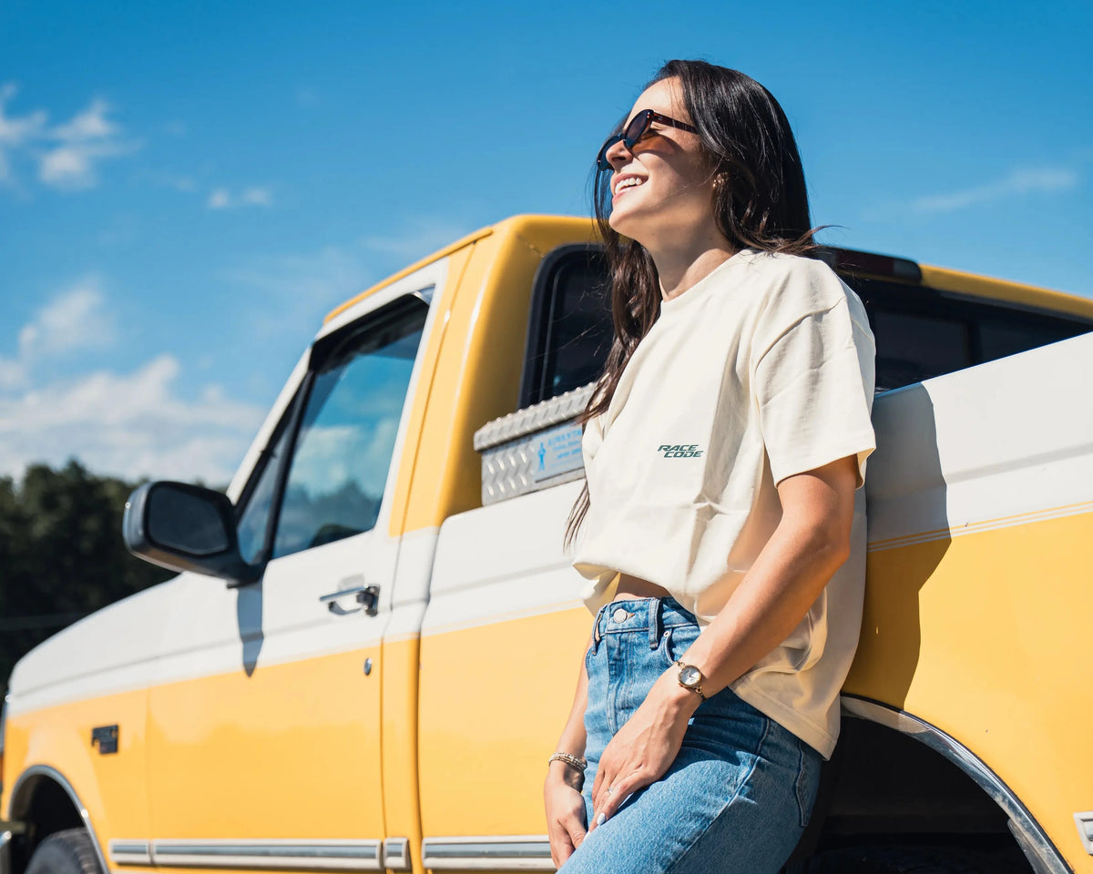 Woman leaning against a yellow and white truck on a sunny day