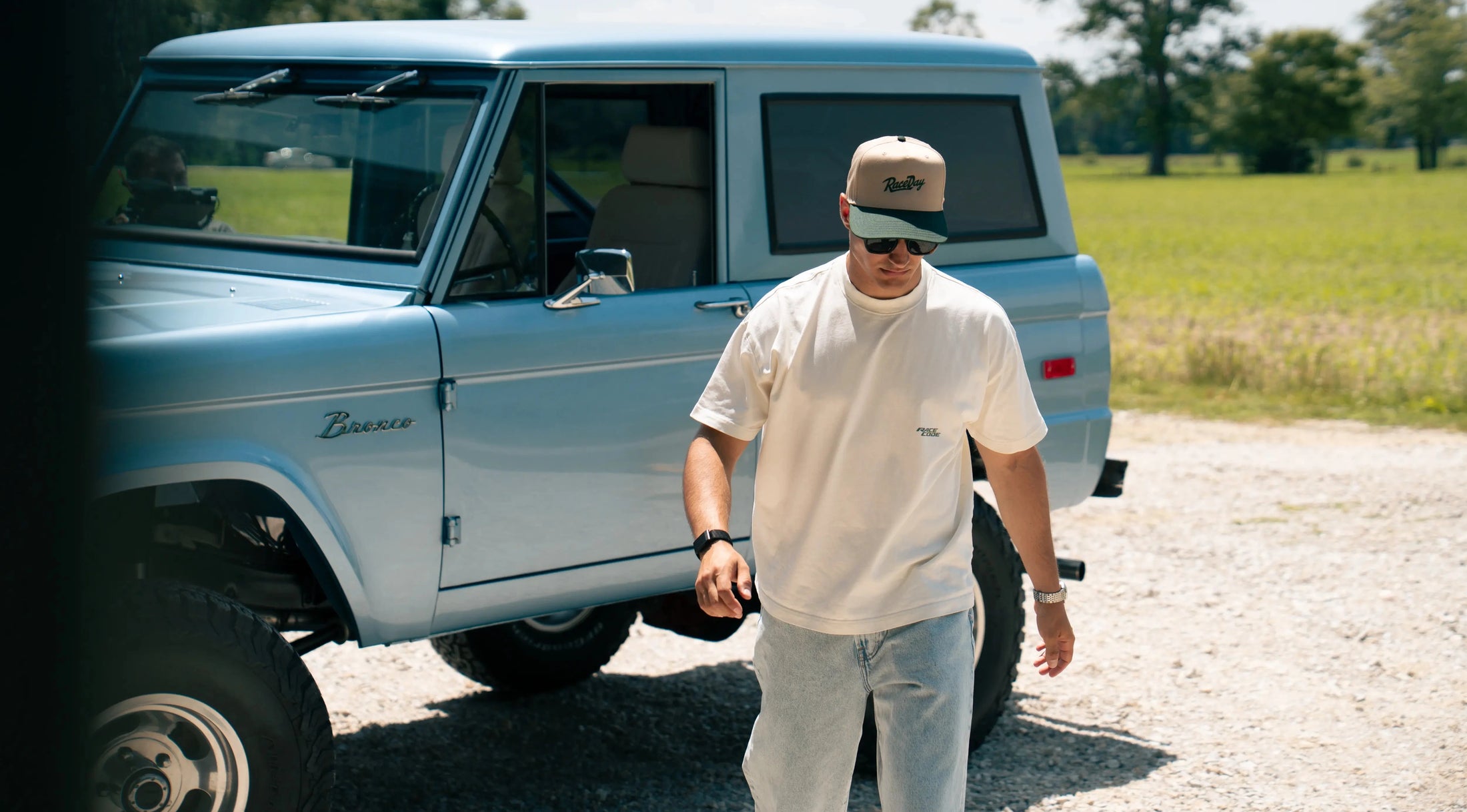 Man standing next to a vintage Ford Bronco in a rural setting