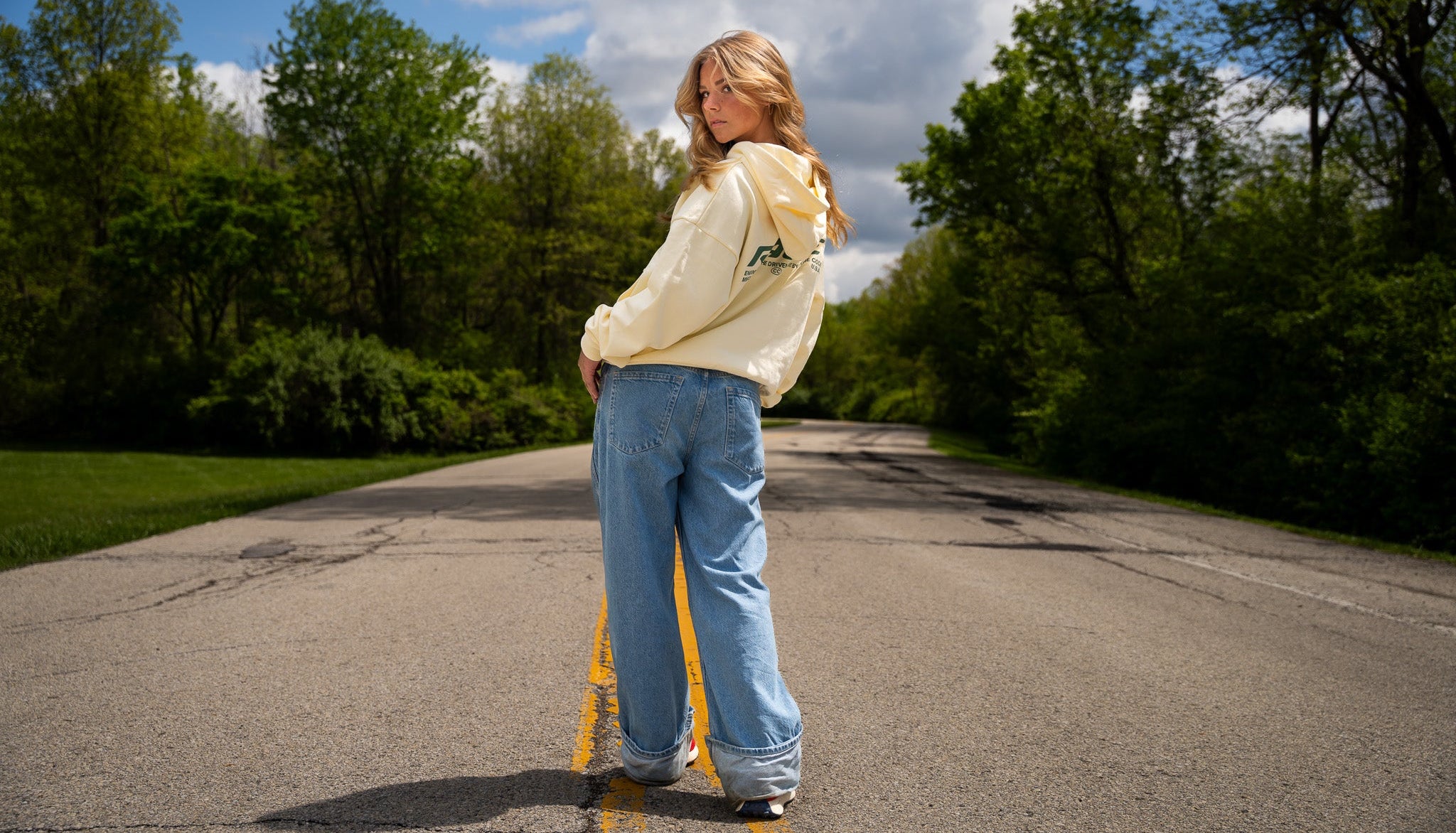 Person standing on a road with trees and a blue sky in the background