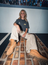 Model sitting on a brick floor wearing the Garage Tee Dark Grey