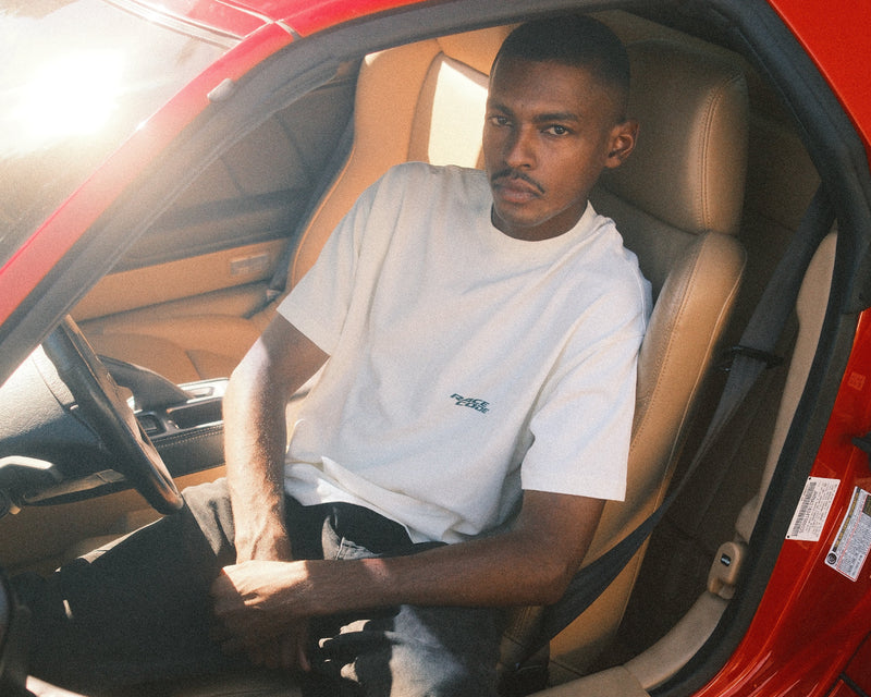 Driver wearing a Race Code tee inside a vintage car — motorsport streetwear in its element